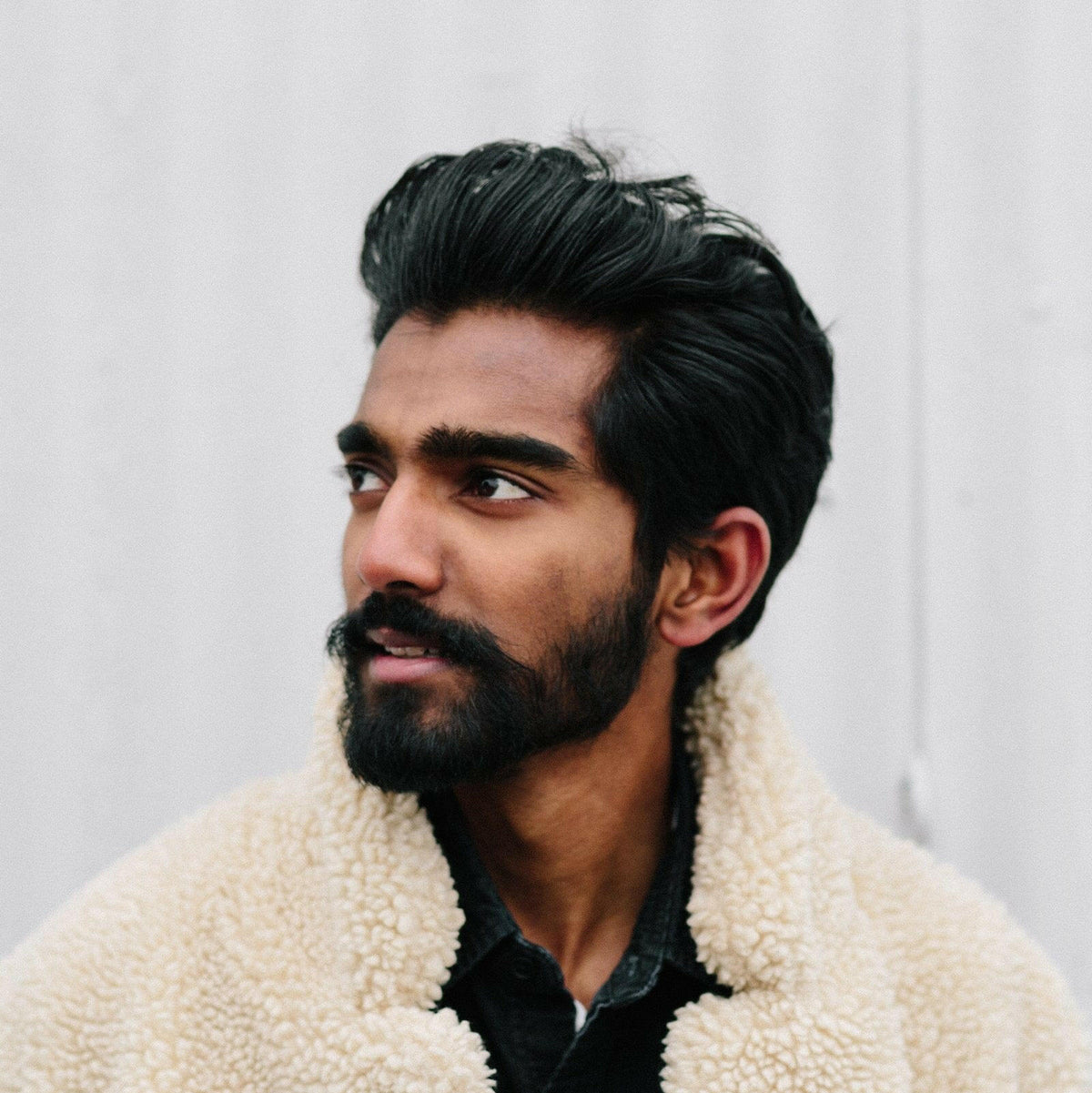 Stylish man wearing a cream sherpa jacket against a plain background