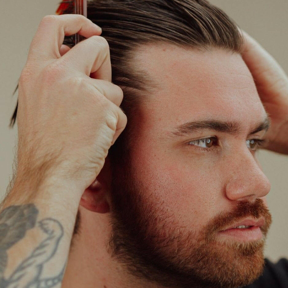 Tattooed man combing his hair against a neutral background.