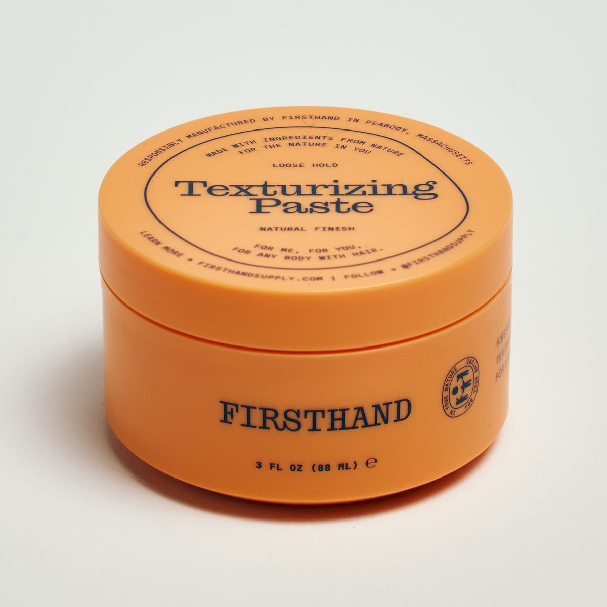 FIRSTHAND Texturizing Paste in a round orange jar with a matching lid, photographed on a clean white background.