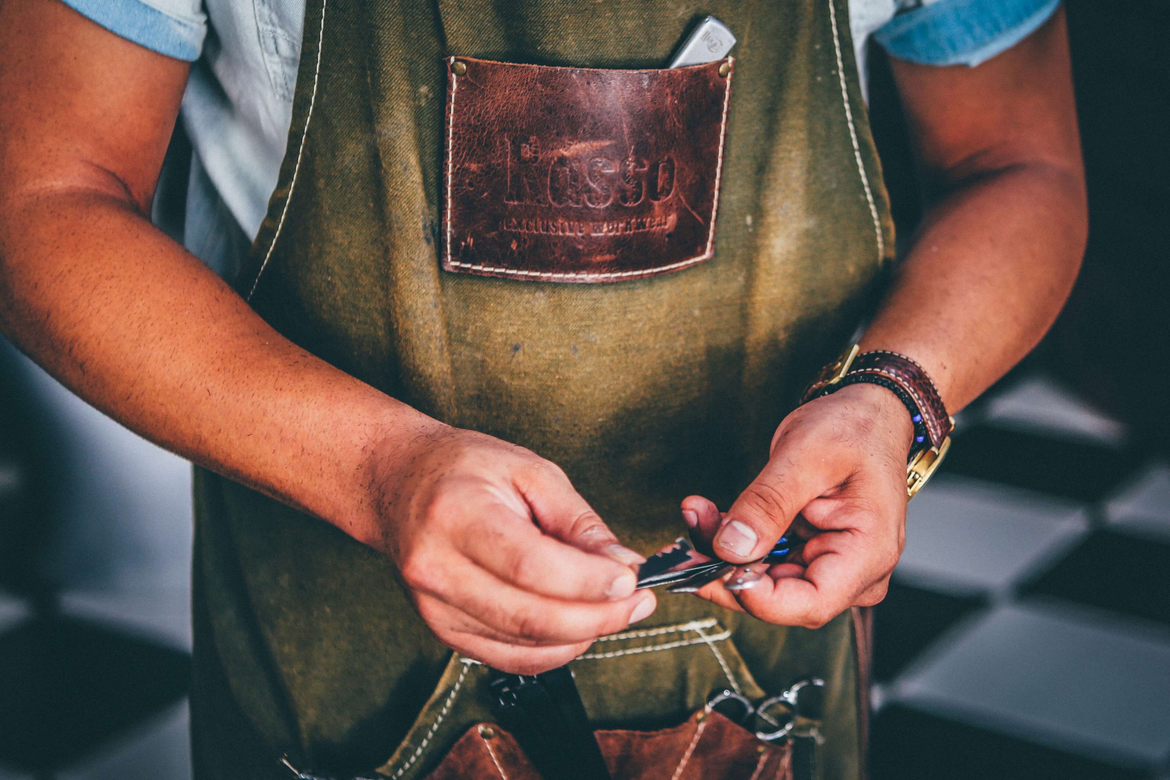Person wearing a green apron with a leather patch, holding a tool.