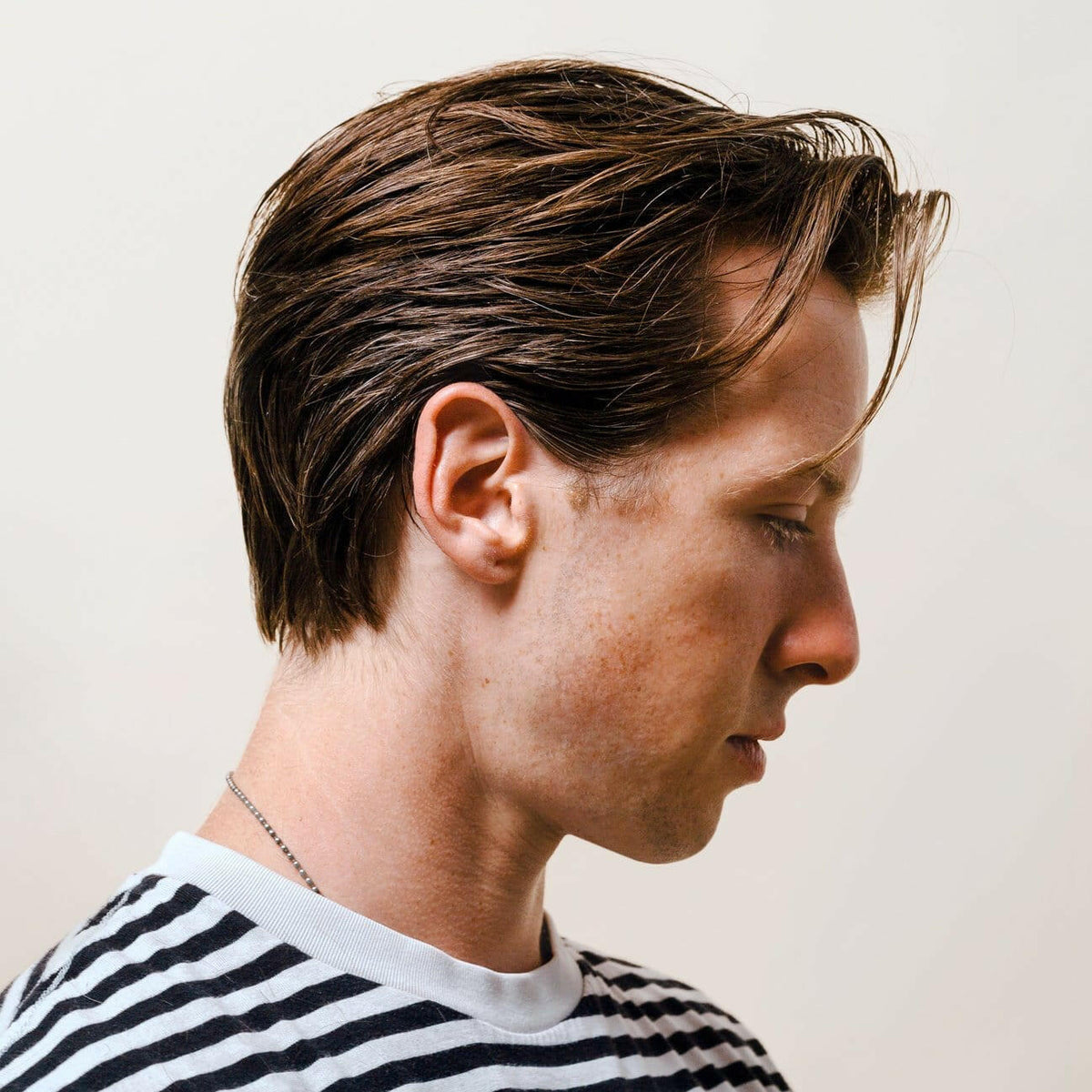 Side profile of a person with short brown hair wearing a black and white striped shirt against a plain background